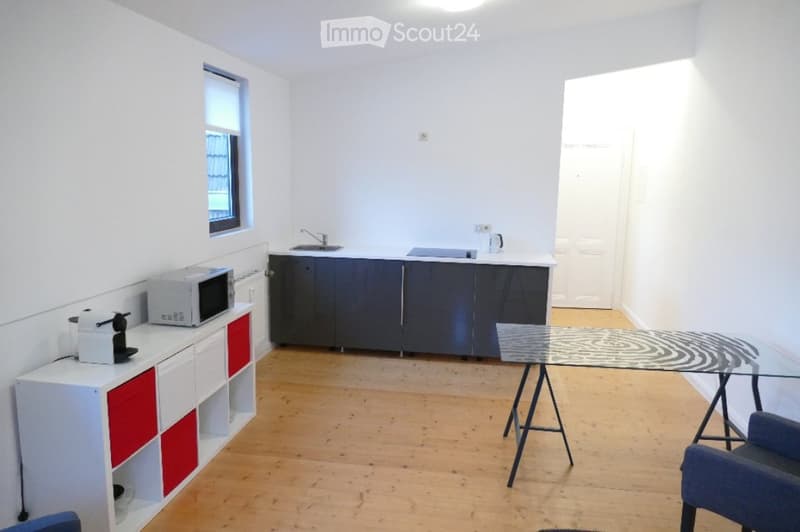 A modern, minimalist kitchen with white and red cabinets, a microwave, coffee maker, sink, and a glass dining table with chairs.