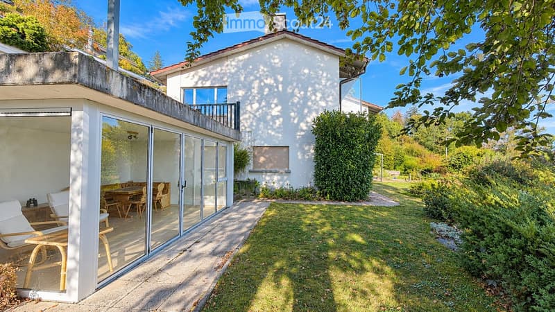 Two-story house with a modern design, featuring a balcony, a patio area with outdoor furniture, and a well-maintained garden.