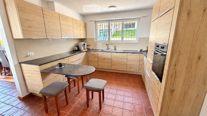 Modern kitchen with wooden cabinets, granite countertop, sink, oven, coffee maker, and a small round table with two stools.