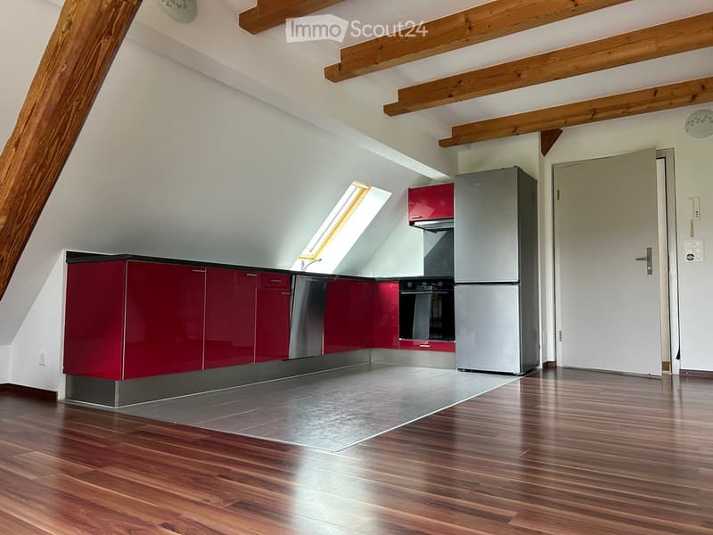 Empty kitchen with red cabinets, stainless steel appliances, wooden ceiling beams, and a window.
