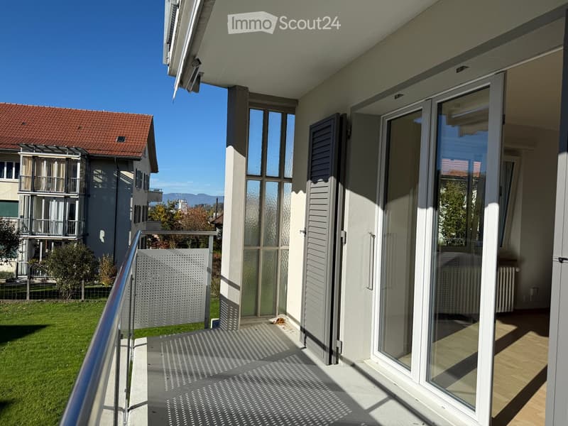 Balcony with glass doors, metal railing, and view of a grassy area and neighboring building.