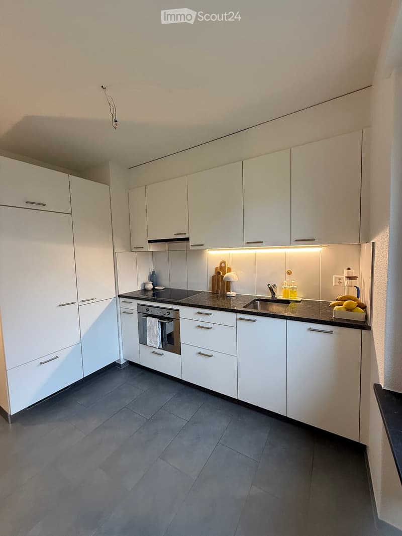 Modern kitchen with white cabinets, dark countertops, and stainless steel appliances. Includes an oven, sink, and various small items on the counter.