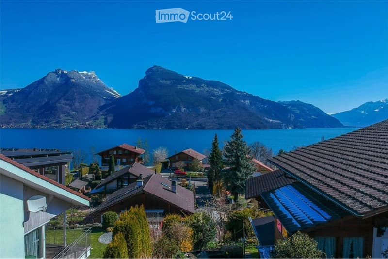 Scenic view of a lakeside village with houses, surrounded by mountains and a clear blue lake.