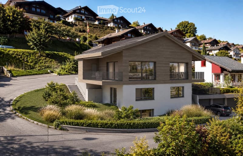 Modern two-story house with wooden facade, large windows, and balconies, surrounded by greenery and other houses in a hilly neighborhood.