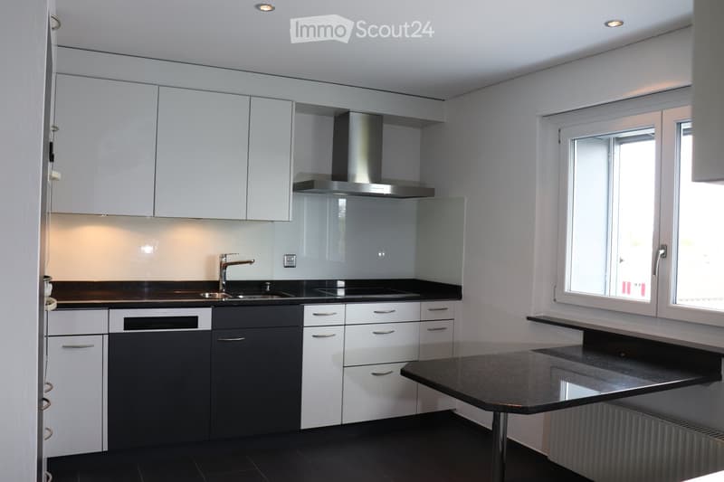 Modern kitchen with white and grey cabinets, black countertops, stainless steel sink and faucet, built-in oven, and large windows.