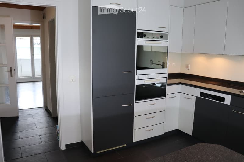 Modern kitchen with white and dark grey cabinets, built-in oven, dishwasher, and sleek countertops.