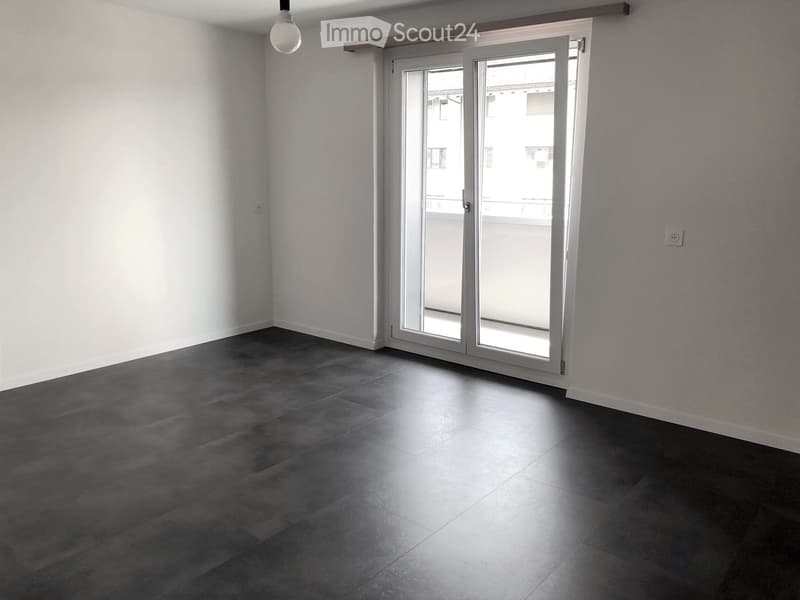 Empty room with grey tiled floor, white walls, and large sliding glass doors leading to a balcony.