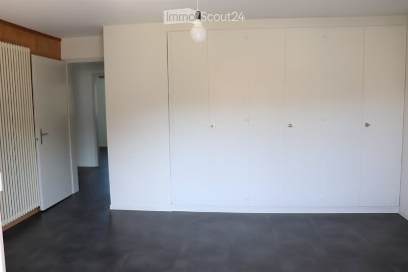 Empty room with white walls, dark grey tiled floor, built-in white wardrobes, and a hanging light fixture.