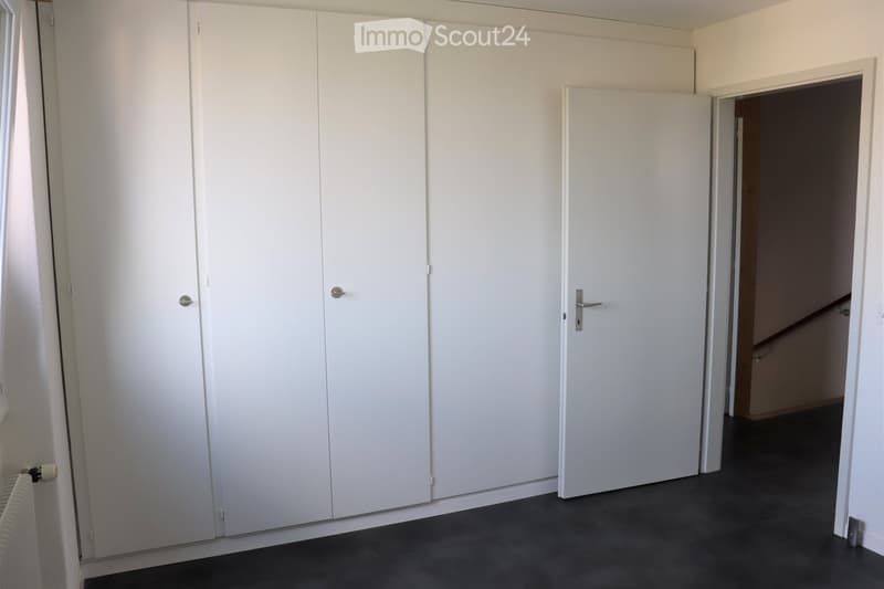 Empty room with white built-in wardrobes, dark flooring, and a radiator visible on the left side.