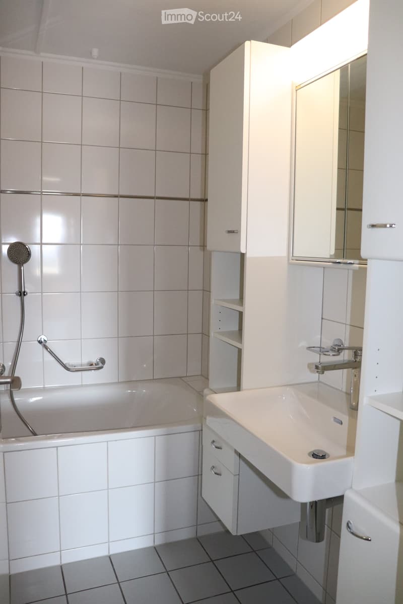 Modern bathroom with white tiles, a bathtub, a sink, a mirror, and white cabinets.