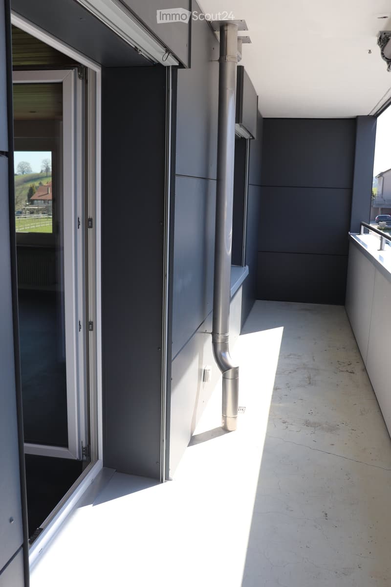 Modern balcony with concrete floor, white walls, and a view of the countryside through large glass doors.