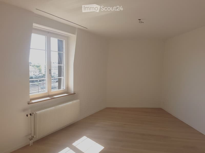Empty room with wooden flooring, white walls, large window with radiator below, and bright natural light.
