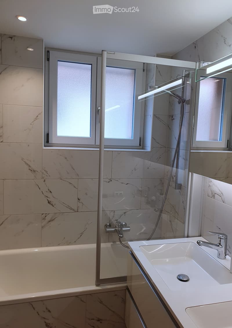 Modern bathroom with marble tiles, a bathtub, a sink with a modern faucet, a glass shower enclosure, and a large mirror.