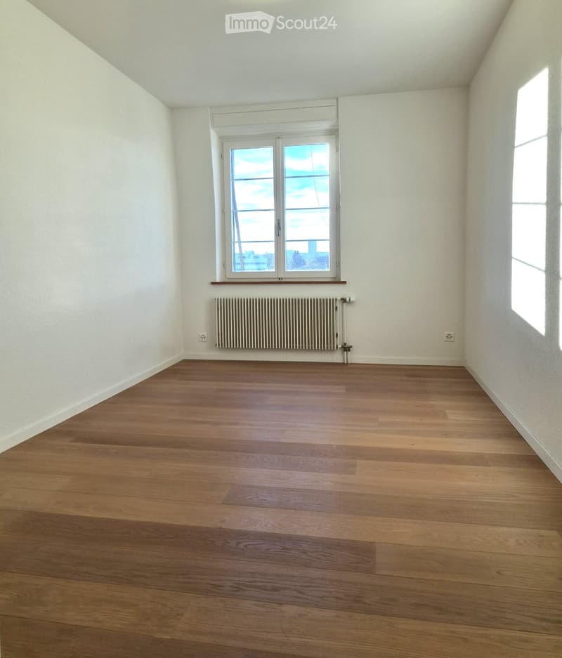 Empty room with wooden flooring, white walls, and a window with a radiator below it.