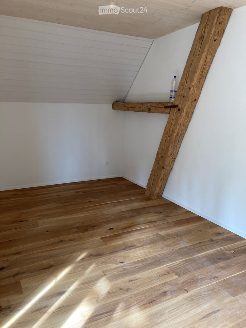 Empty room with wooden flooring and white walls, featuring a wooden shelf on the wall with a single bottle placed on it.