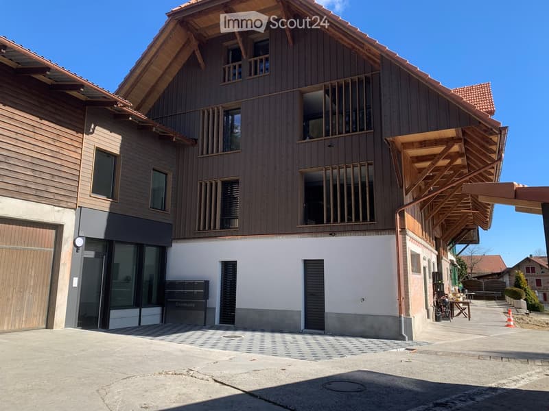 Modern two-story wooden building with large windows, balconies, and a covered entrance area.