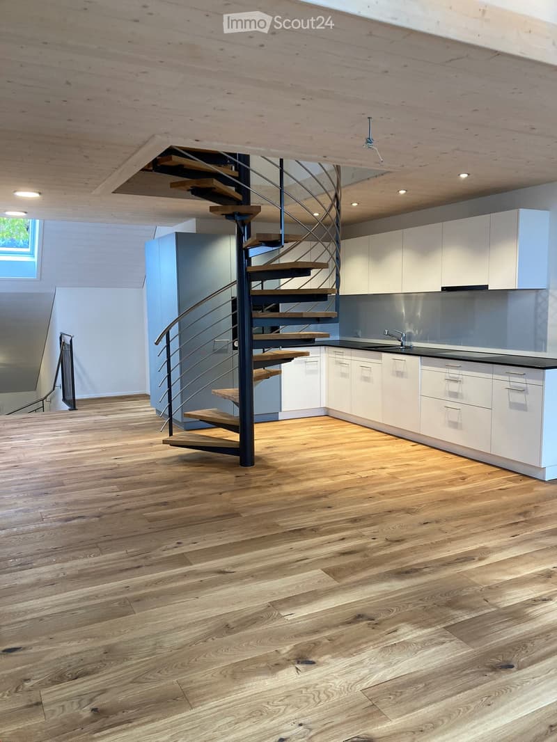 Open-plan space with wooden flooring, white kitchen cabinets, a modern staircase with wooden steps and metal railing, and a sink area.