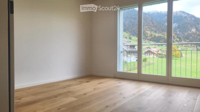 Empty room with wooden flooring and large windows offering a scenic mountain view.