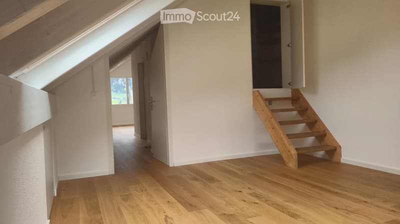 Bright, airy hallway with wooden flooring, white walls, and a wooden staircase leading upwards. Skylight and open doorway visible.