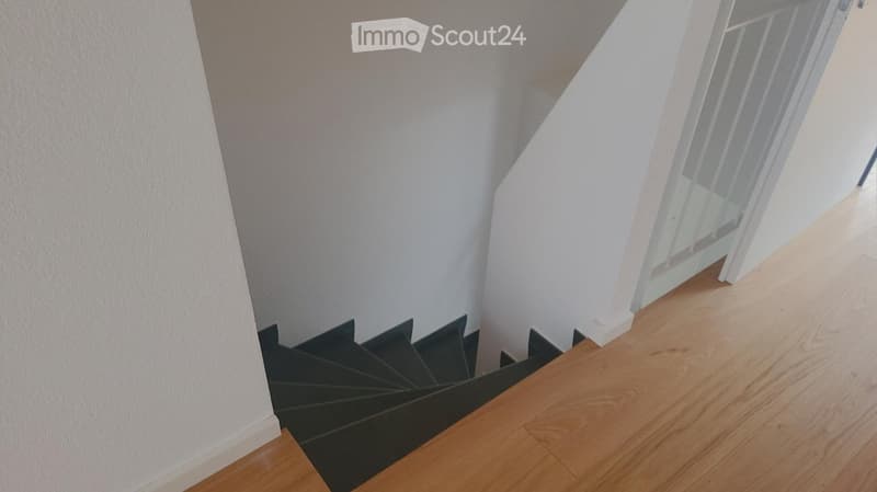 A modern staircase with wooden steps and black railings, leading up against white walls.