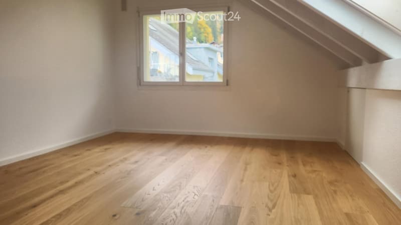 Empty room with wooden flooring and a window showing a view of neighboring buildings.
