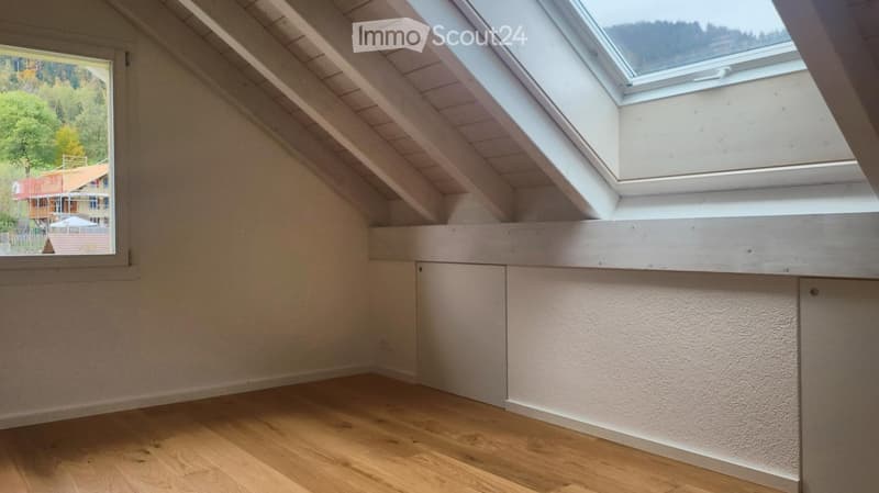 Empty attic room with wooden flooring, white walls, and skylight window. No furniture or equipment present.