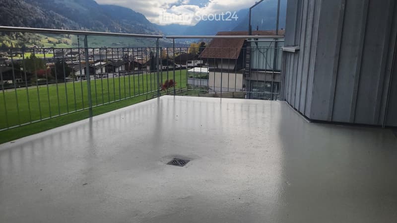 Balcony with a metal railing, overlooking a green valley and distant mountains.