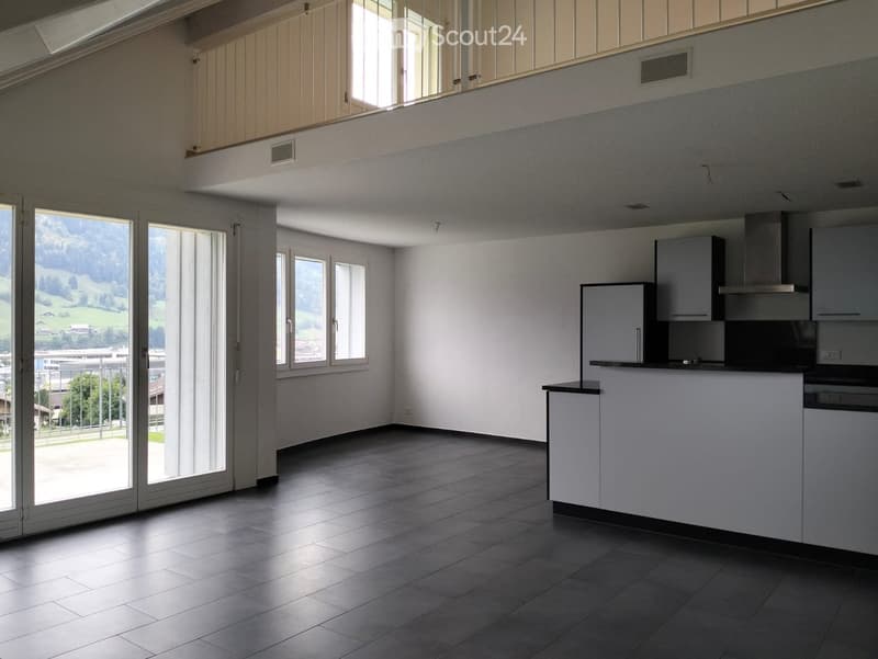 Empty kitchen with dark tiled floor, white cabinets, and large windows overlooking a scenic landscape.