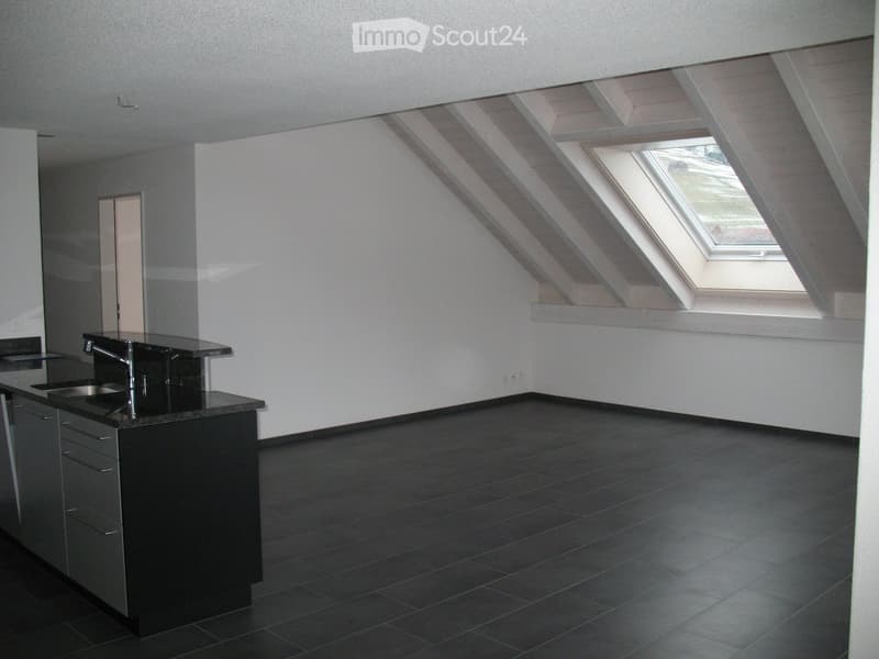 Modern kitchen with dark countertops, stainless steel sink, and cabinets. Features a skylight window and dark tiled flooring.