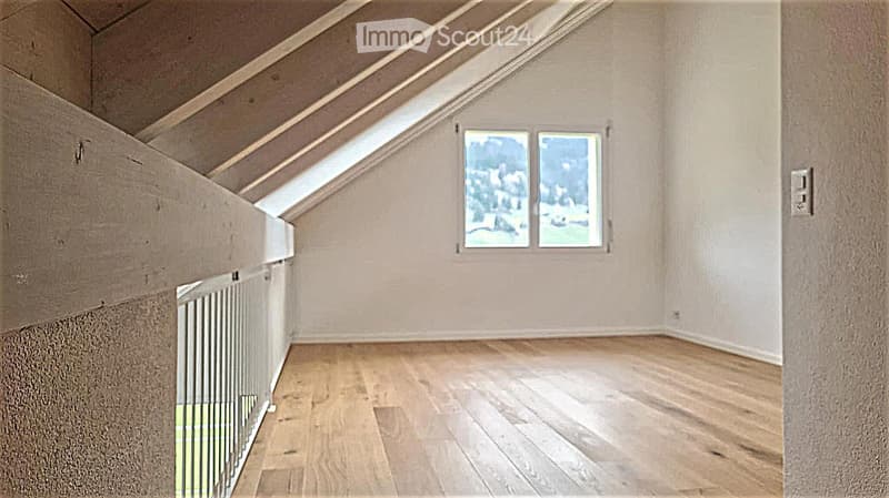 Empty attic room with wooden flooring, white walls, and skylight windows, featuring exposed wooden beams on the ceiling.