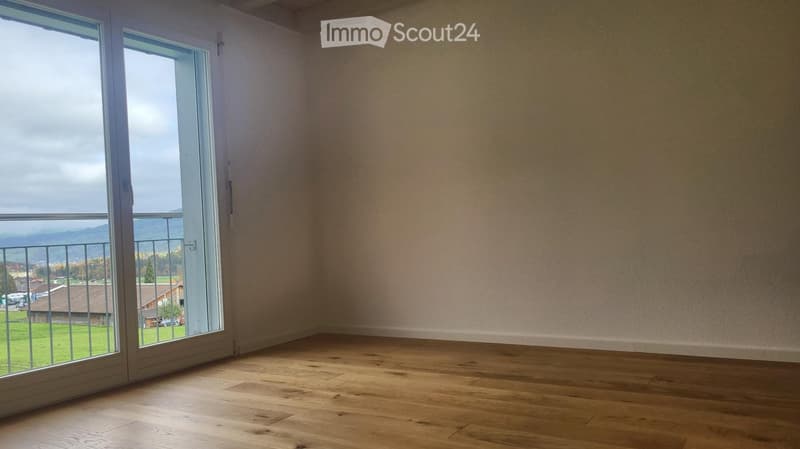 Empty room with wooden flooring, large window offering a scenic view of the countryside and mountains.