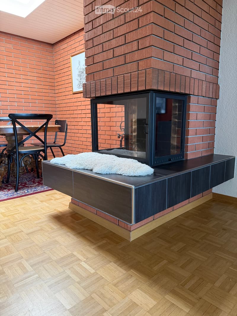 Modern living room with a brick fireplace, wooden floor, and a small seating area with a table and chairs.