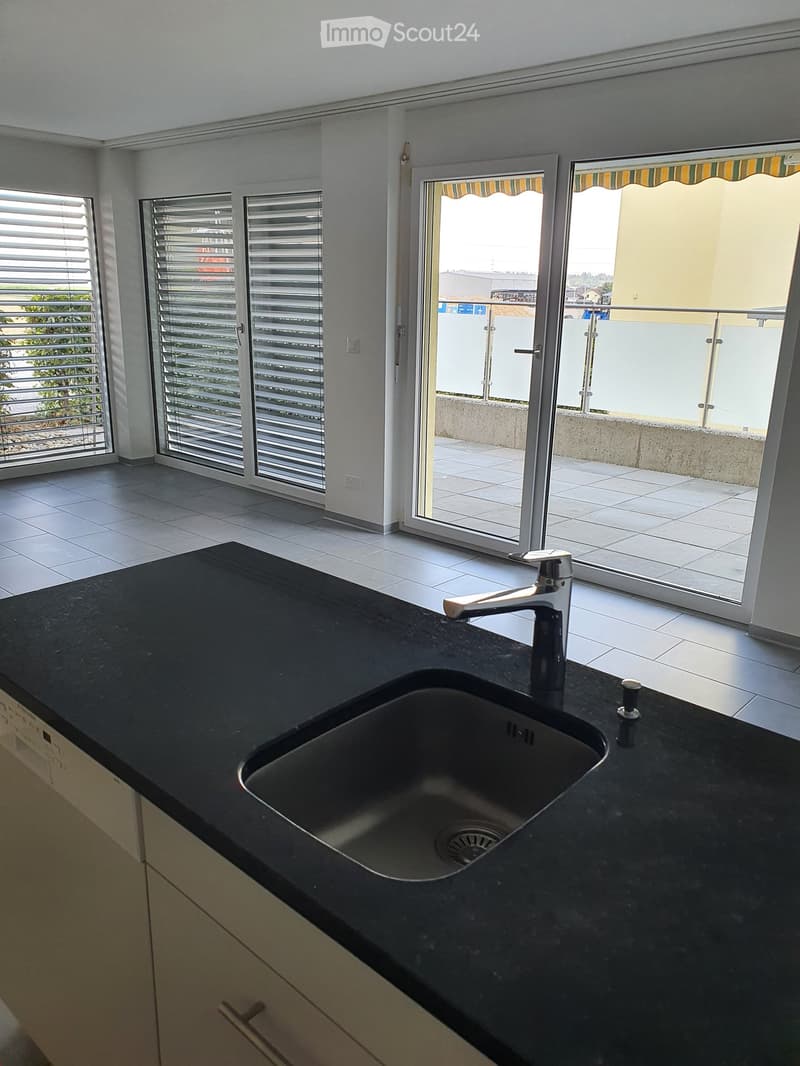 Modern kitchen with black granite countertop, stainless steel sink, and large windows with blinds leading to a balcony.