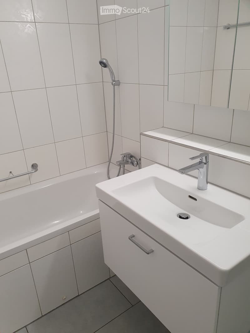 Modern bathroom with white tiles, a bathtub, a sink with a modern faucet, and a large mirror above the sink.