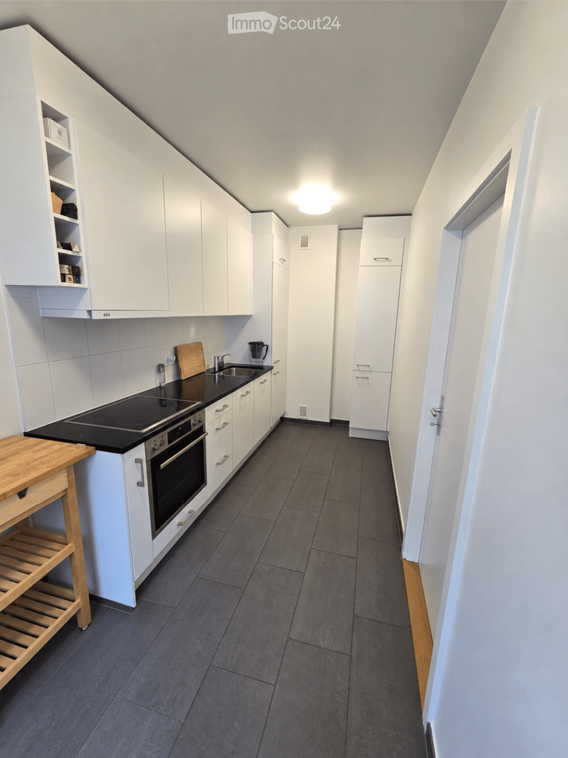 Modern kitchen with white cabinets, black countertop, built-in oven, sink, and wooden shelf.