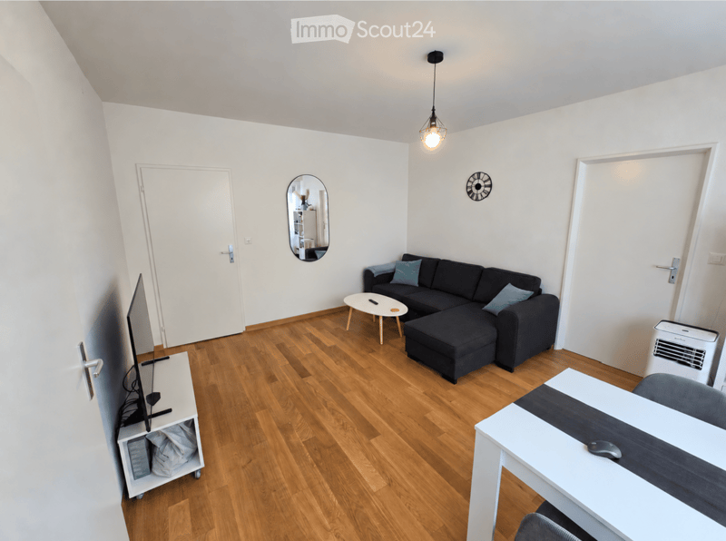 Modern living room with wooden flooring, a black sectional sofa, a white coffee table, a TV stand, a desk, and an air conditioner.