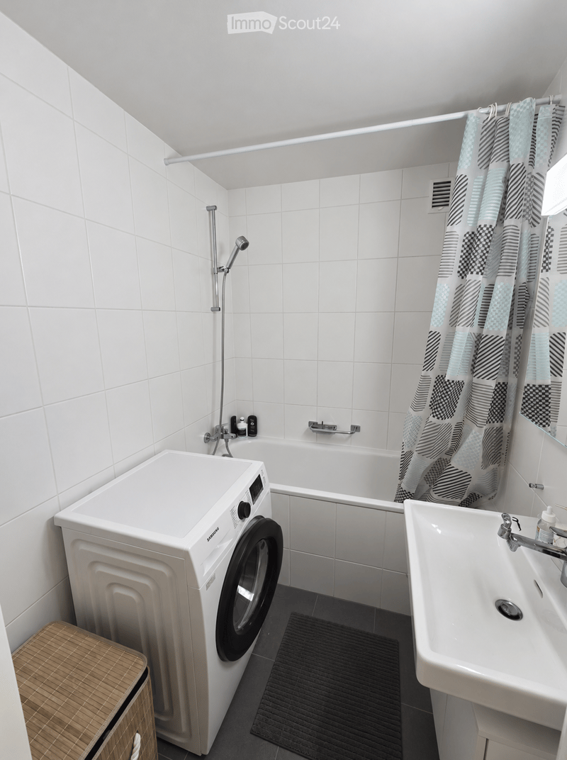 Modern bathroom with white tiles, a washing machine, bathtub, sink, shower curtain, and a wicker basket.