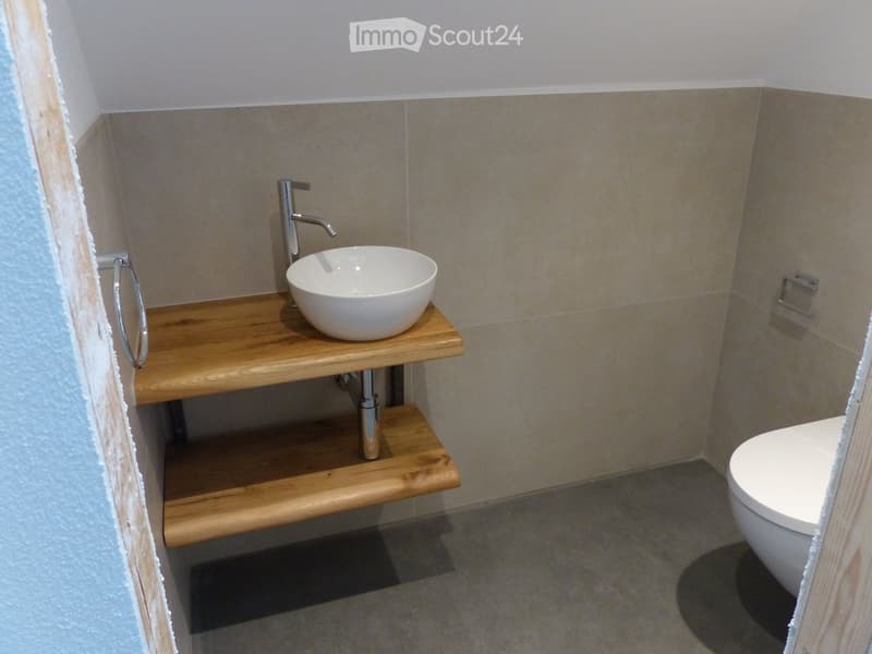 Modern bathroom with a wooden shelf holding a white sink bowl and faucet, a toilet, and a towel ring on the wall.