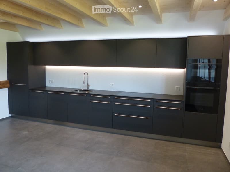 Modern kitchen with dark grey cabinets, stainless steel sink, and built-in oven. Exposed wooden beams on the ceiling.