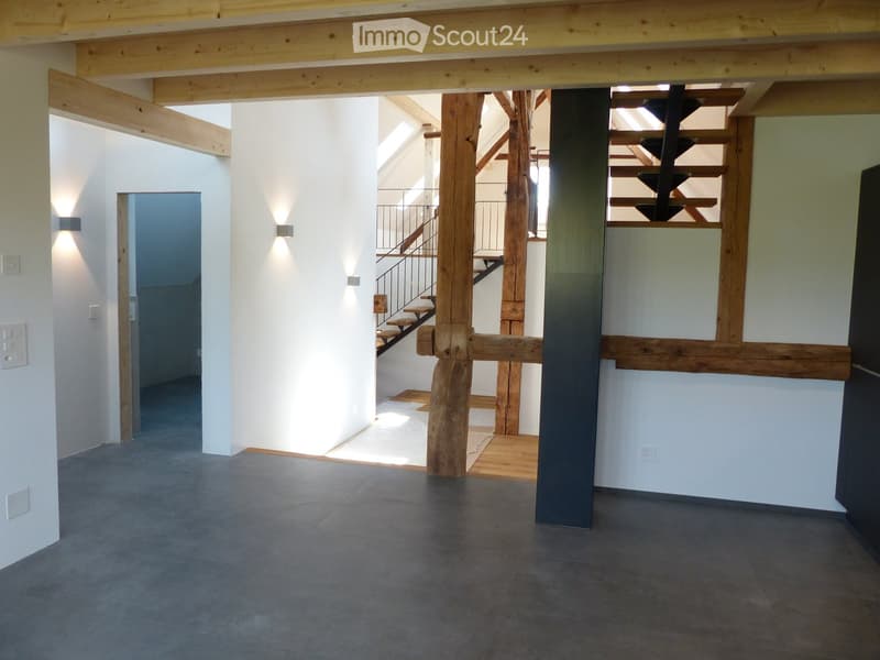 Open hallway with exposed wooden beams, concrete floor, and a staircase leading to an upper level.