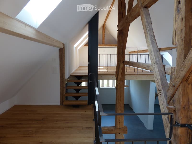 Staircase with wooden steps and metal railing, leading to an upper level with exposed wooden beams and skylight windows.