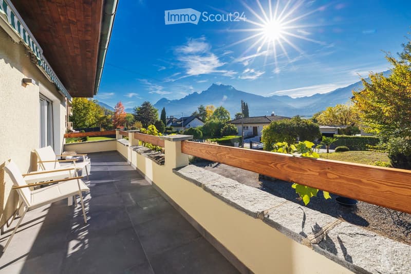 Balcony with wooden railing, tiled floor, white chairs, and scenic mountain view.