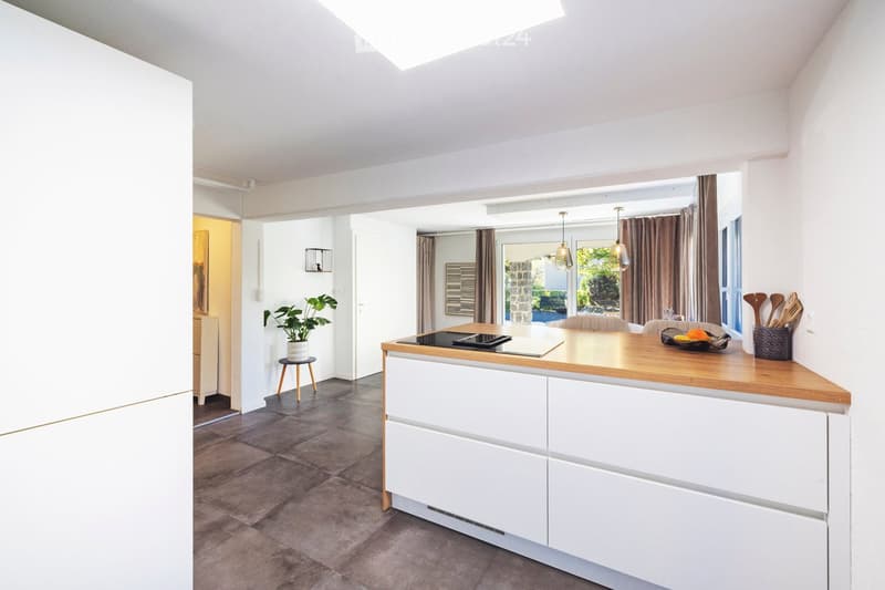 Modern kitchen with white cabinets, wooden island, induction cooktop, pendant lights, and a small plant on a stool.