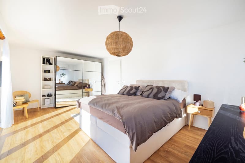 Modern bedroom with a large bed, nightstands, a wooden chair, a mirror, and a shelf with accessories.