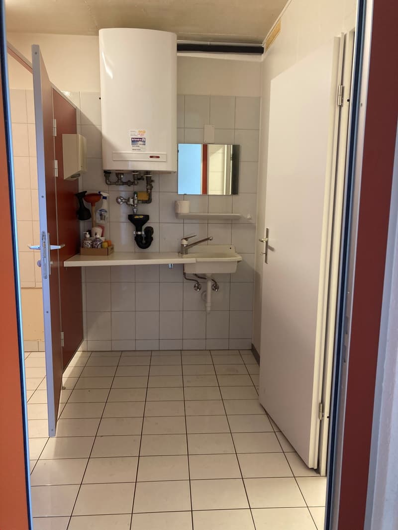 A small bathroom, tiled floor, sink, mirror, open door, water heater