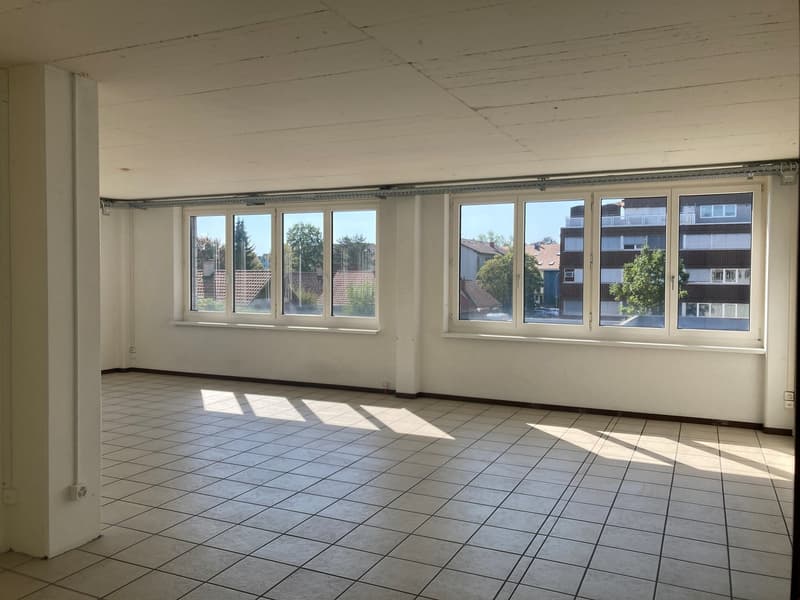 Empty room with white tile flooring, windows overlooking outside view, neutral wall and ceiling.