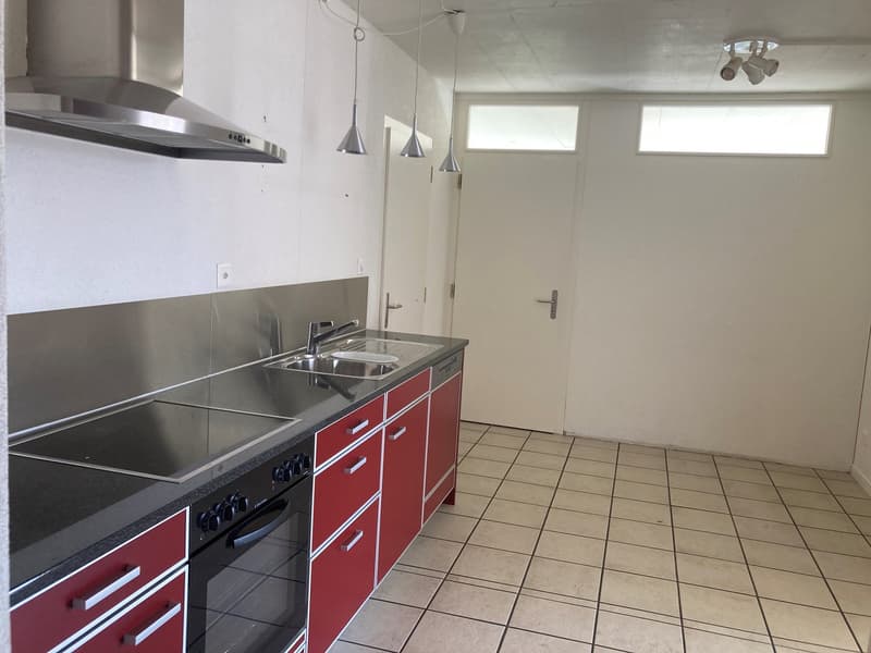 empty kitchen with steel appliances, sink, gas stove, red cupboards, tiled floor