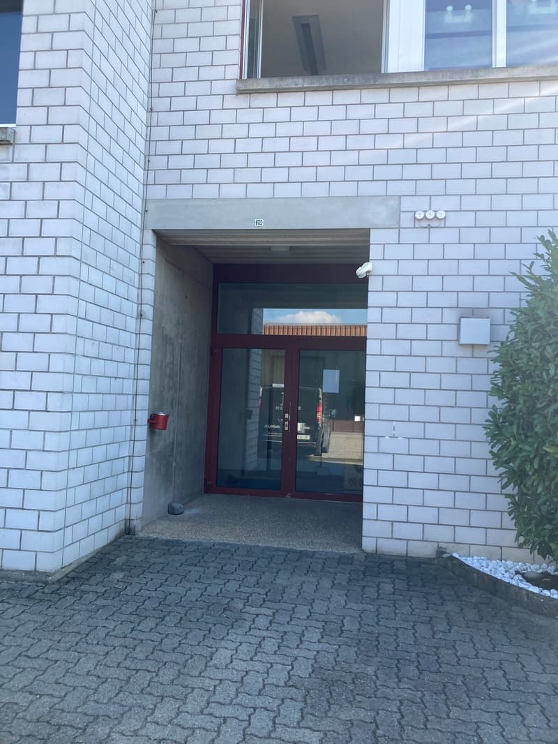 Entrance area with brick wall and glass doors, tiled floor, parking spot