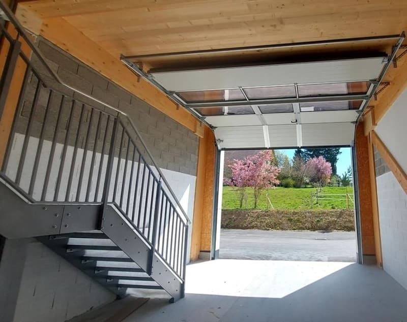 Open garage door, metal handrail, concrete floor, wooden ceiling, view of a grassy field