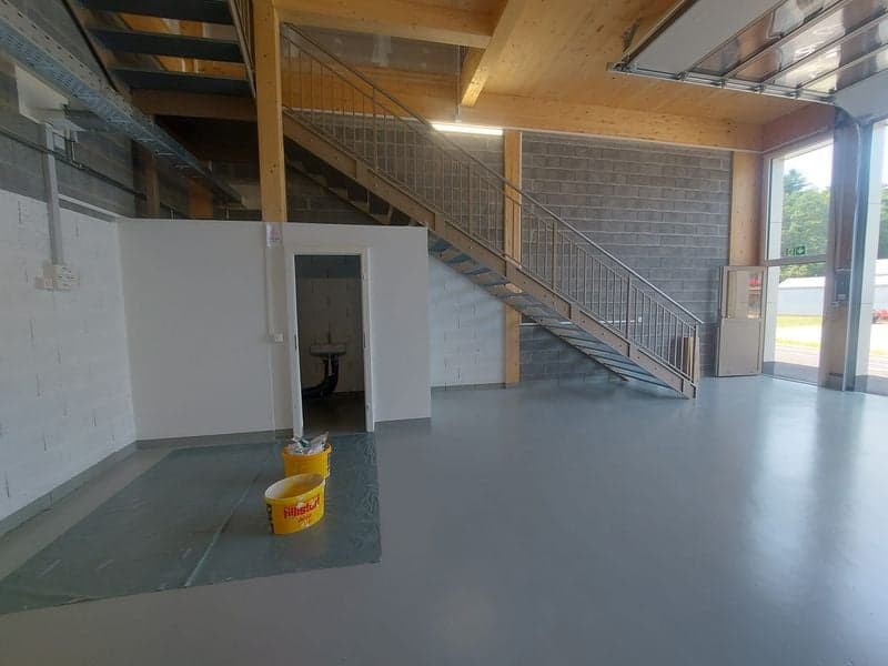 Empty room with concrete floor, white walls, staircase, and a door leading to a small room with a sink.